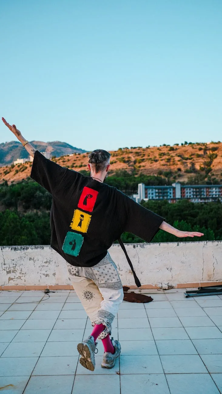 A man in a black shirt with colorful design dances energetically on a rooftop. — Photo : armağan başaran (Pexels License) via Pexels